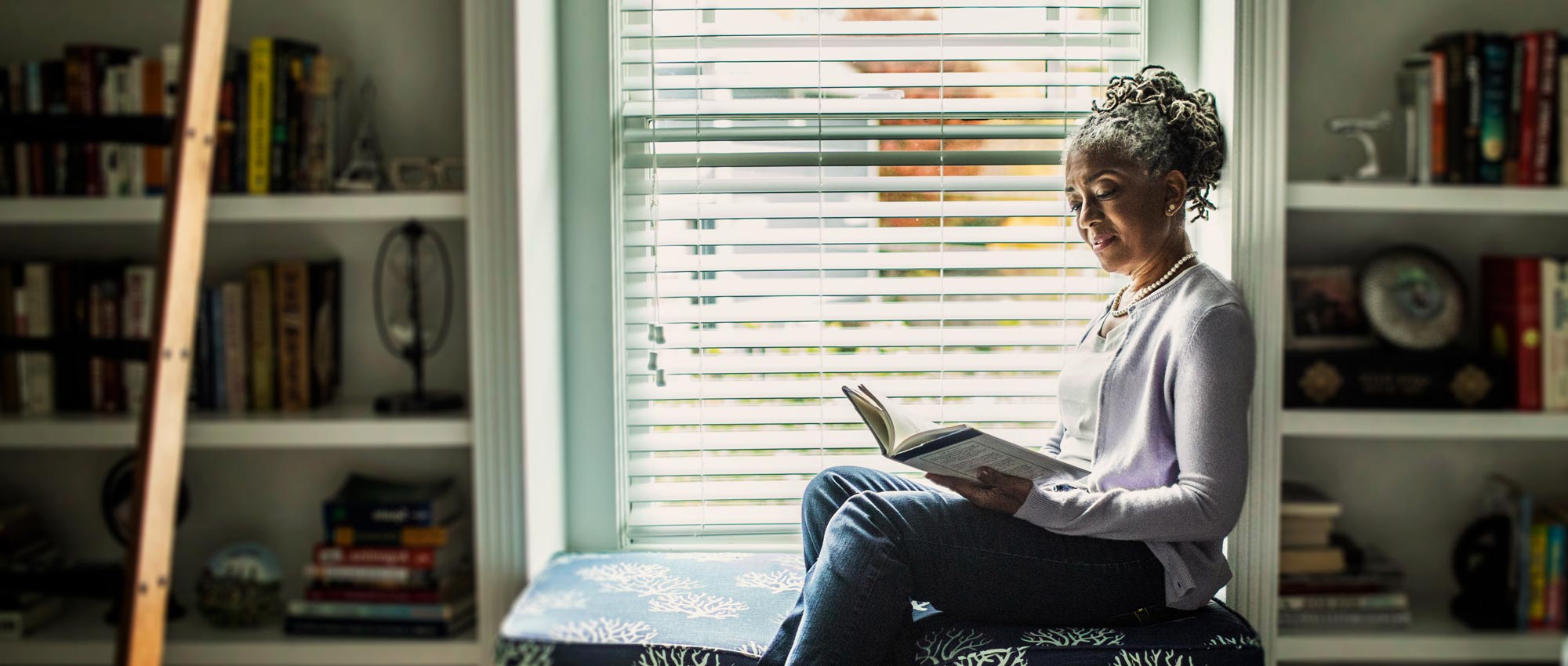 A woman is sitting reading a book next to a window